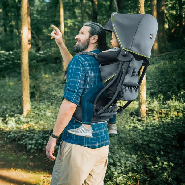 Man carrying a child in a backpack carrier through a forest