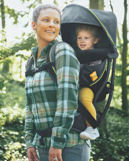 Woman carrying a child in a backpack carrier through a forest
