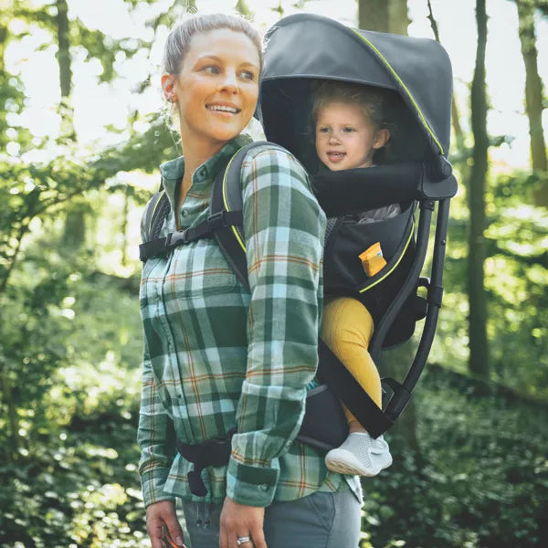 Woman carrying a child in a backpack carrier through a forest
