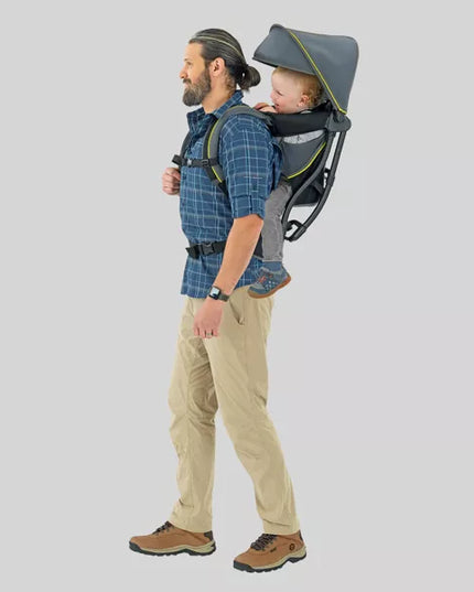 Man carrying a child in a backpack carrier on a plain background