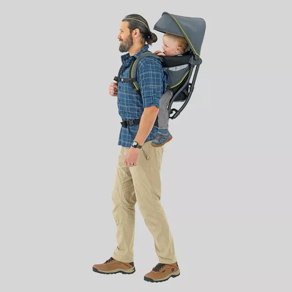 Man carrying a child in a backpack carrier on a plain background