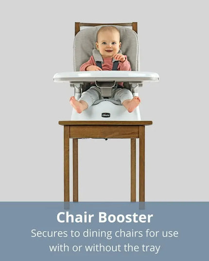 Baby in a chair booster seat on a wooden chair with a gray background