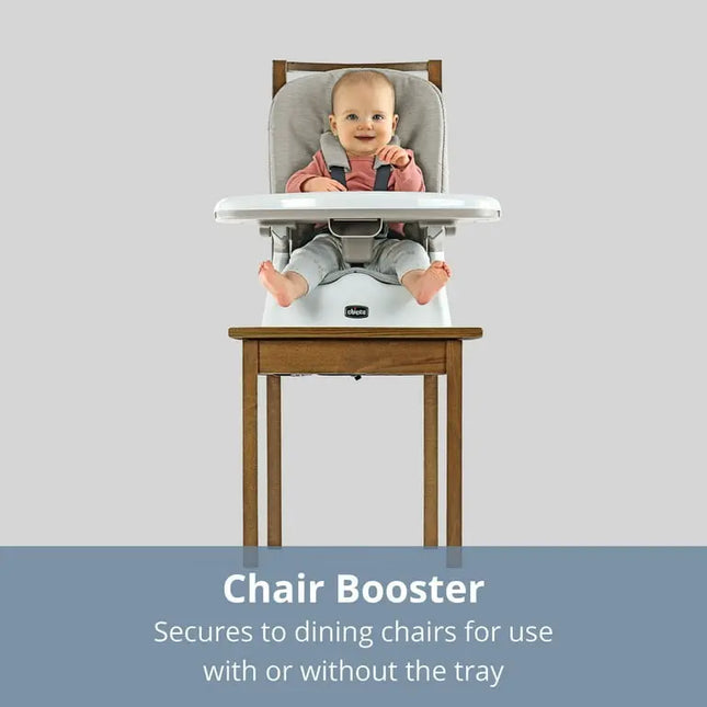 Baby in a chair booster seat on a wooden chair with a gray background