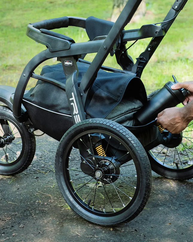 Black All-Terrain Stroller with a person adjusting a component outdoors.