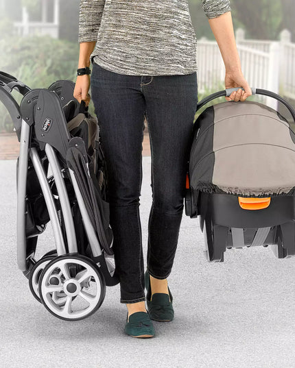 Person holding a stroller and a baby carrier on a light surface
