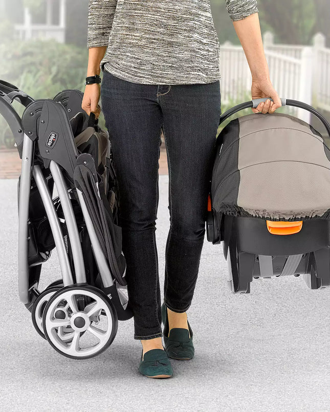 Person holding a stroller and a baby carrier on a light surface