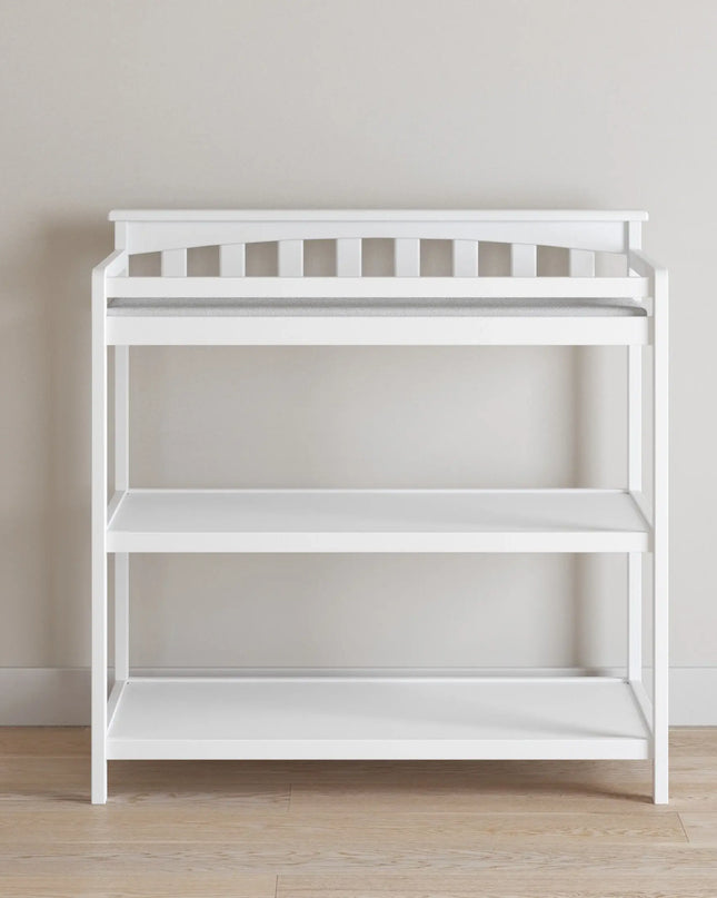 White changing table with shelves against a plain wall.