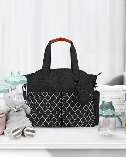 Black diaper bag with patterned design on a white surface with baby items around