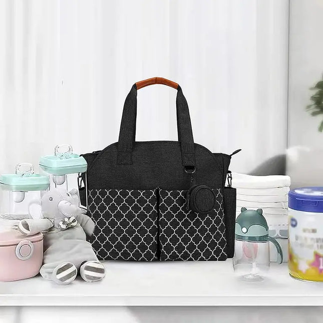 Black diaper bag with patterned design on a white surface with baby items around