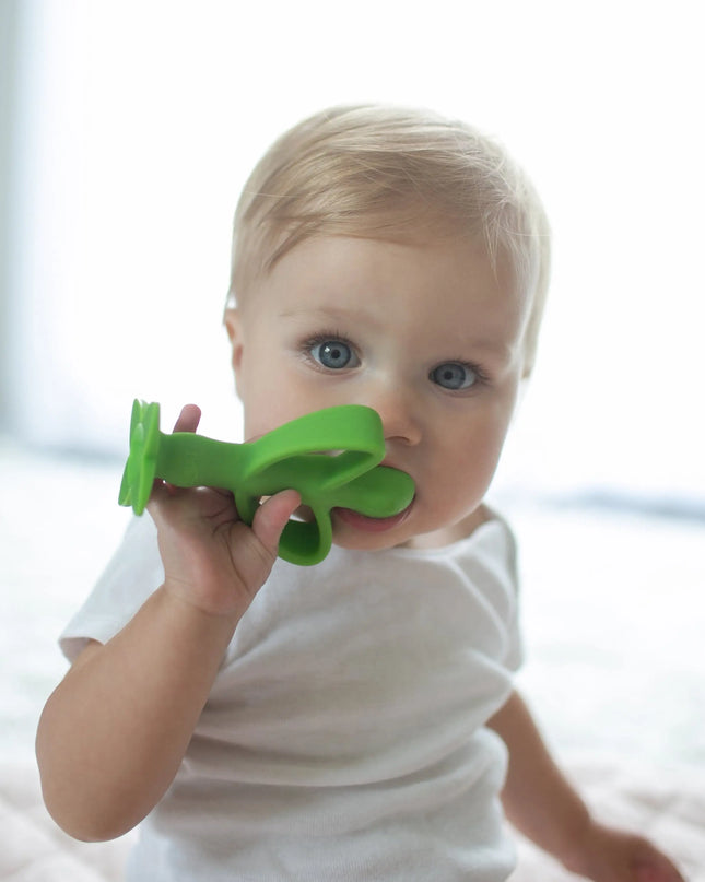 Baby holding a green teething toy against a blurred background