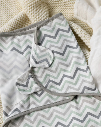 Folded blanket with gray and green chevron pattern on a textured surface