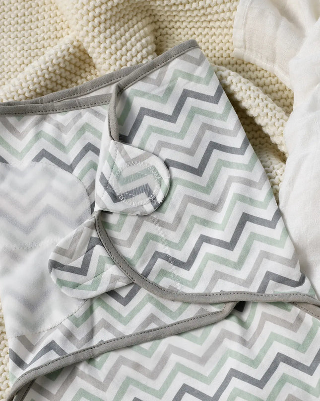 Folded blanket with gray and green chevron pattern on a textured surface