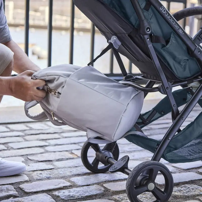 Gray backpack with wheels attached to a stroller on a paved walkway.