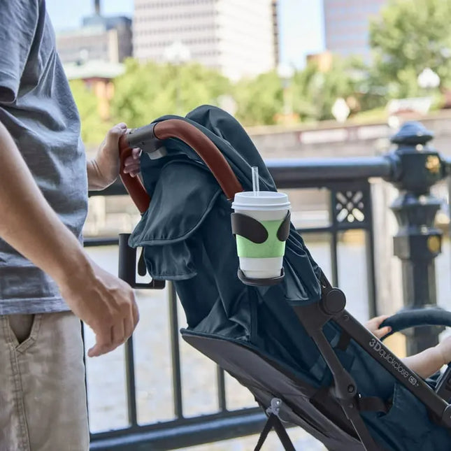 Stroller with a cup holder attached, featuring a drink with a green sleeve and brown lid.