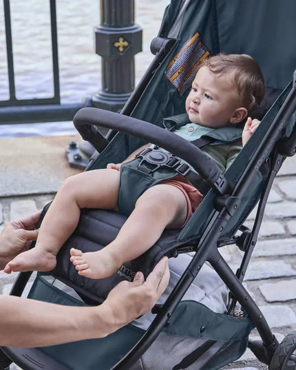 Child in a stroller being adjusted by an adult outdoors.
