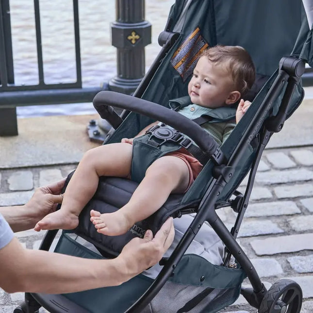Child in a stroller being adjusted by an adult outdoors.