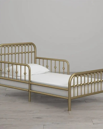 Gold metal bed frame with white mattress and pillow on a wooden floor.