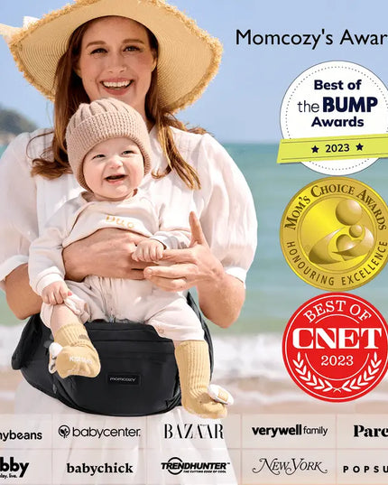 Woman holding a baby in a carrier on a beach with awards displayed.