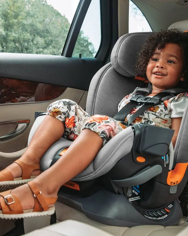 Child sitting in a car seat with a safety harness, smiling.
