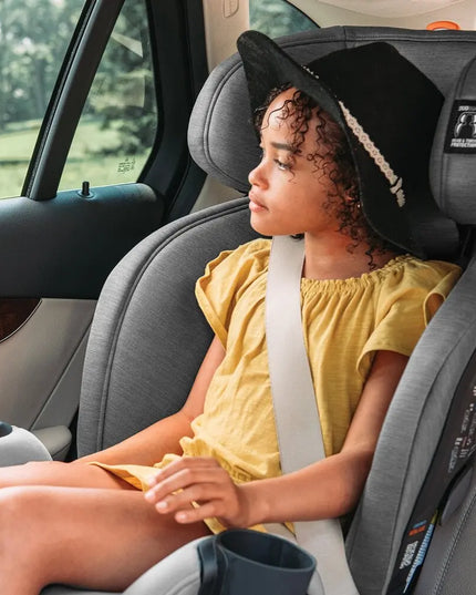 Child in a car seat wearing a yellow shirt and black hat, with a blurred outdoor background