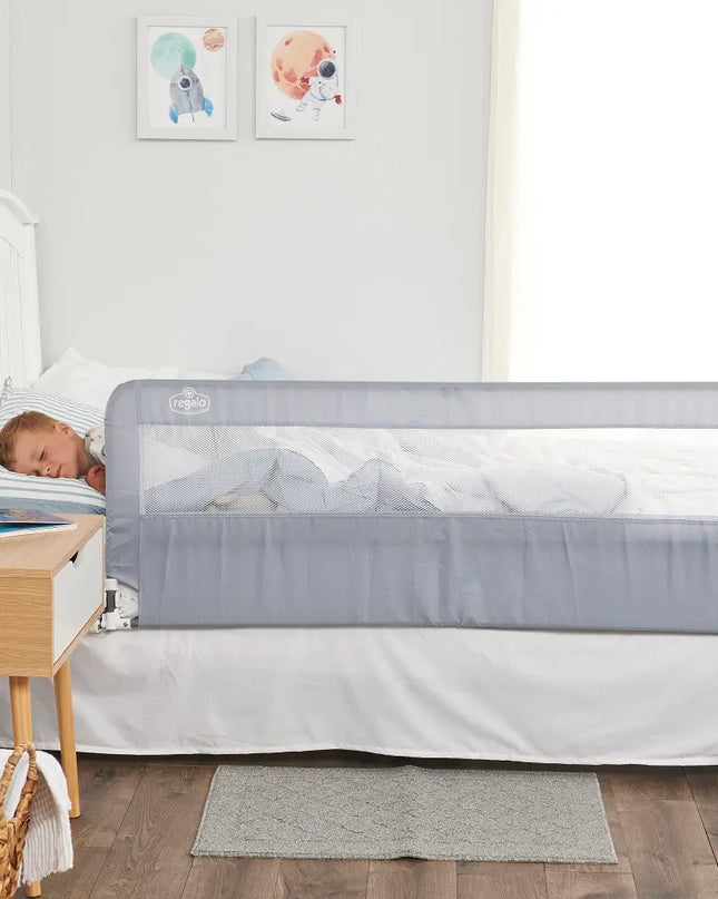 Child sleeping in a crib with a gray safety rail in a bedroom setting.