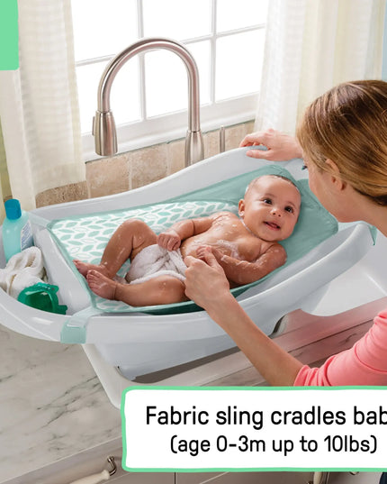 Baby being bathed in a fabric sling with a woman in a bathroom setting.