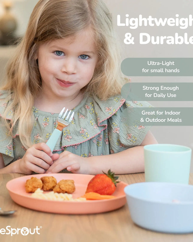 Child eating a meal with cutlery, sitting at a table with a plate of food and a cup.