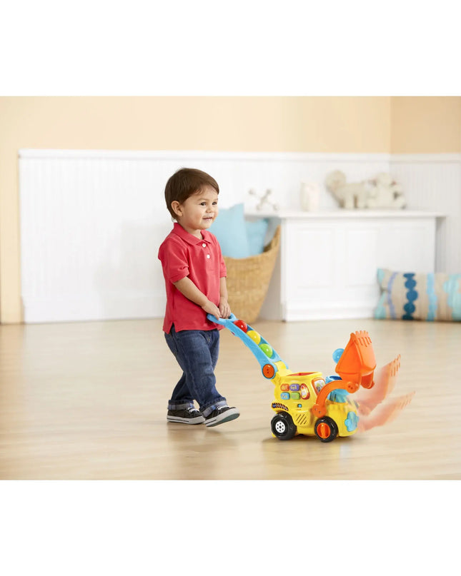 Child playing with a toy bulldozer on a wooden floor.