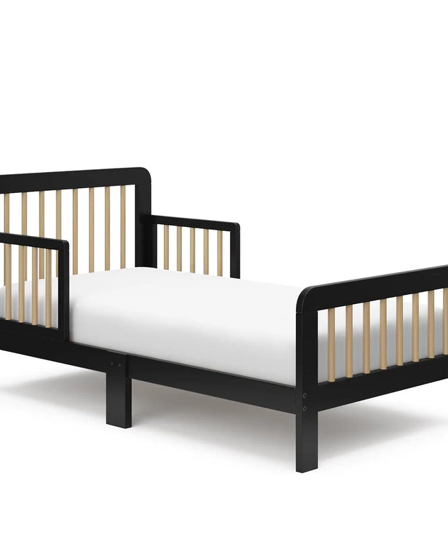 Angled view of the Storkcraft Pasadena toddler bed in a modern nursery setting with soft lighting